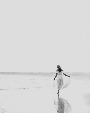 A person in white dress runs along a misty beach shoreline creating a dreamy ethereal scene.