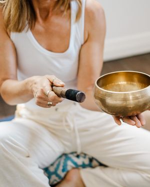 Person in white clothing sits cross-legged with a Tibetan singing bowl for meditation and relaxation practice.