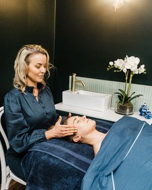 Spa professional performing relaxing facial treatments on client in luxurious treatment room with orchid decor.