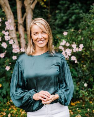 Professional portrait session outdoors with emerald green top against blooming pink flowers in garden setting.
