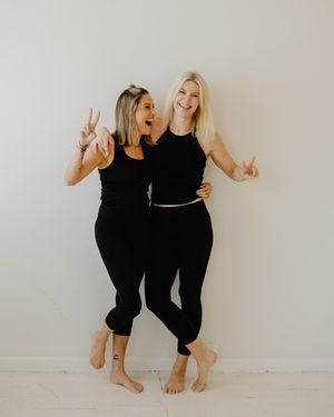 Two women in black outfits strike playful poses against a white wall in a series of candid lifestyle photos.