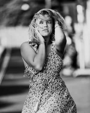 Black and white portrait of a person in a floral dress posing outdoors with windswept hair and expressive pose.