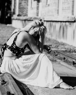 Black and white photo showing someone in a floral top and white skirt sitting outdoors with head bowed down.