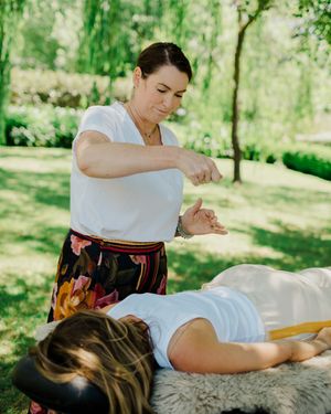 Professional massage therapist performs therapeutic massage treatment on client in outdoor spa setting with lush greenery.
