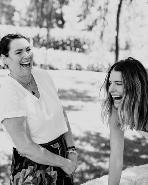 Black and white candid photo of two people sharing a genuine laugh together outdoors in dappled sunlight.