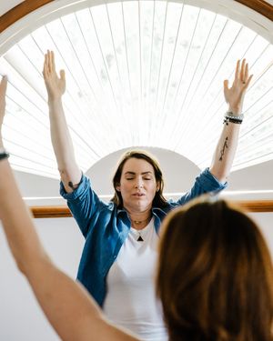 People with raised arms practicing mindfulness or meditation in a bright sunlit room with white walls.