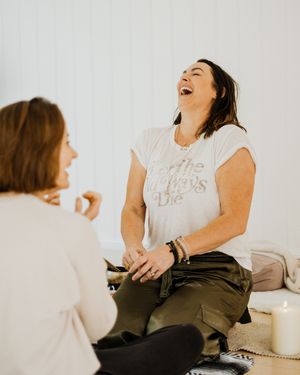 Two people sharing a candid moment of laughter while sitting together against a white background.