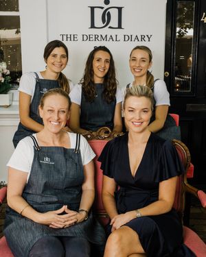 A group of staff members pose together in front of The Dermal Diary storefront sign.