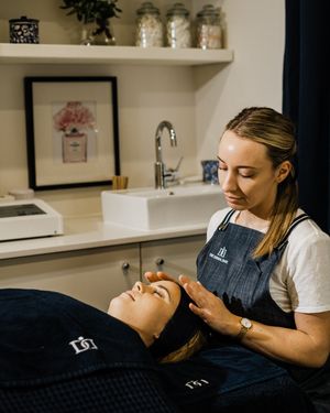 A massage therapist performs facial treatment on a client lying on a treatment table in a spa setting.