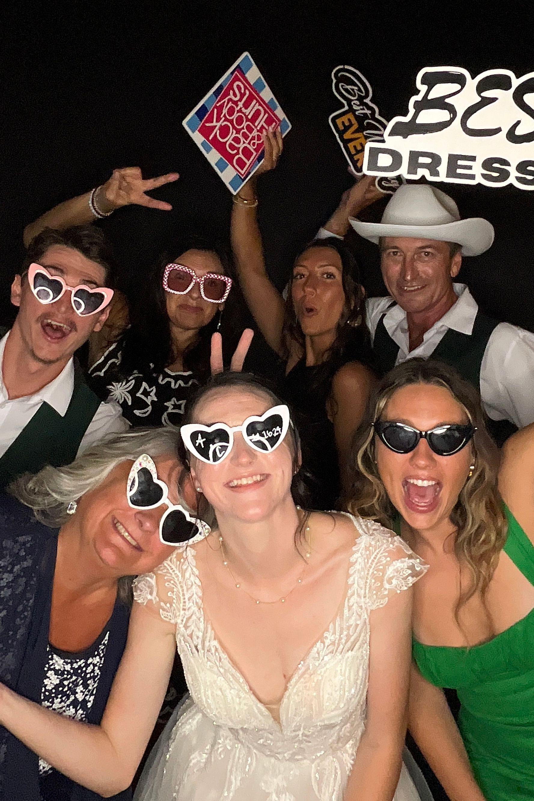 A group of party-goers wearing sunglasses and festive attire pose together in a dark room.