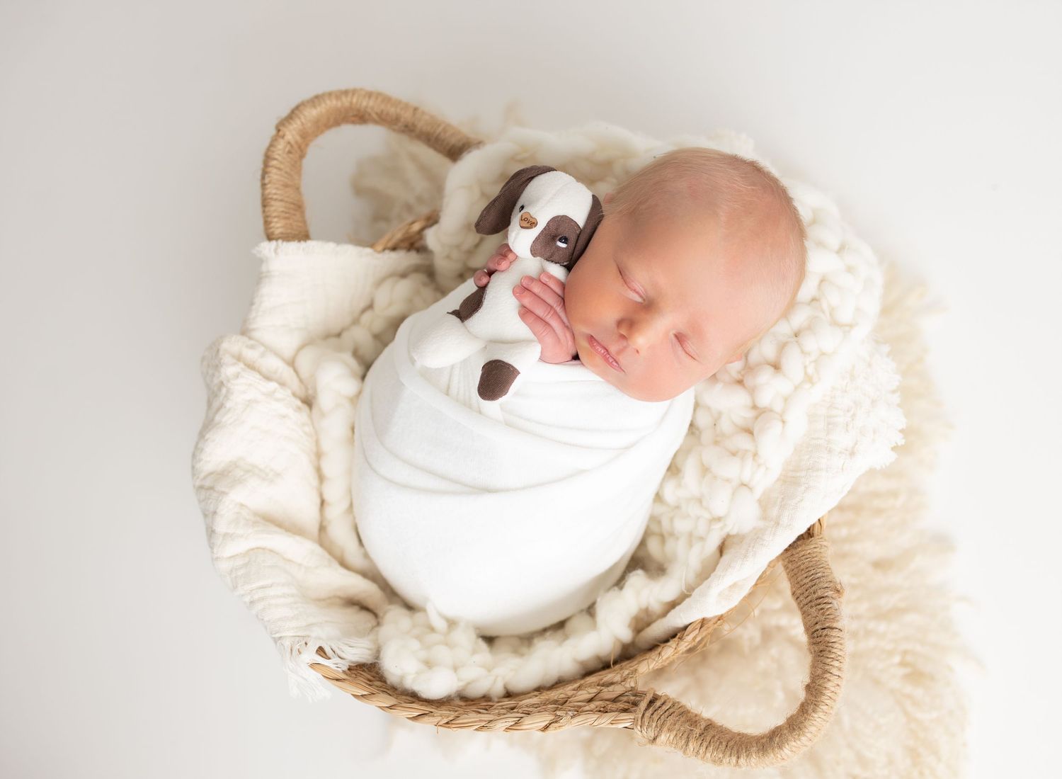 Newborn baby sleeping peacefully on soft cream-colored blankets in a series of gentle poses.