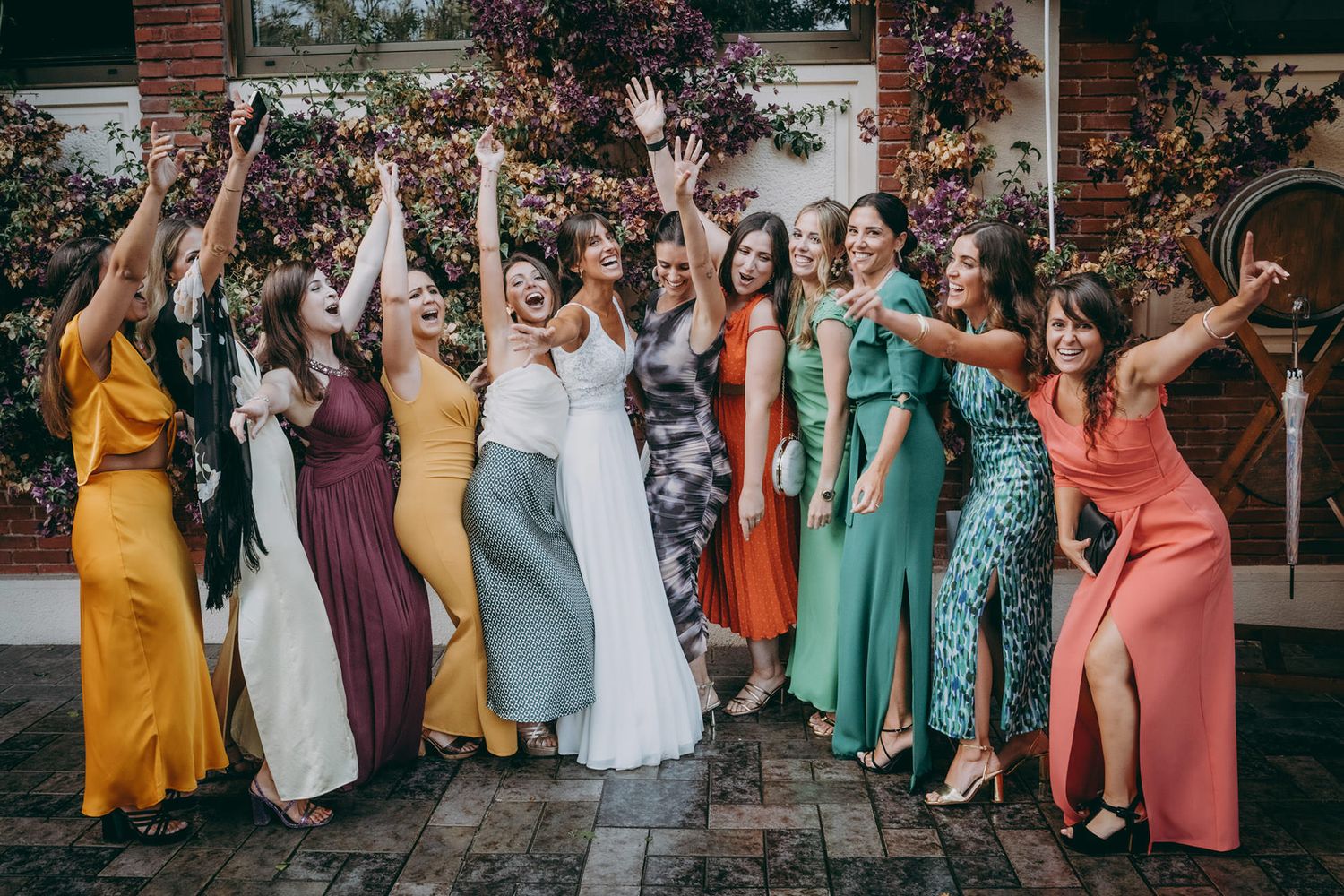 A group of people in colorful dresses pose together for a celebratory outdoor wedding photo shoot.