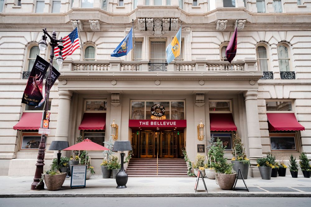 Exterior facade of the luxury Bellevue Hotel with ornate architecture, red awnings, and multiple flags flying above the entrance.