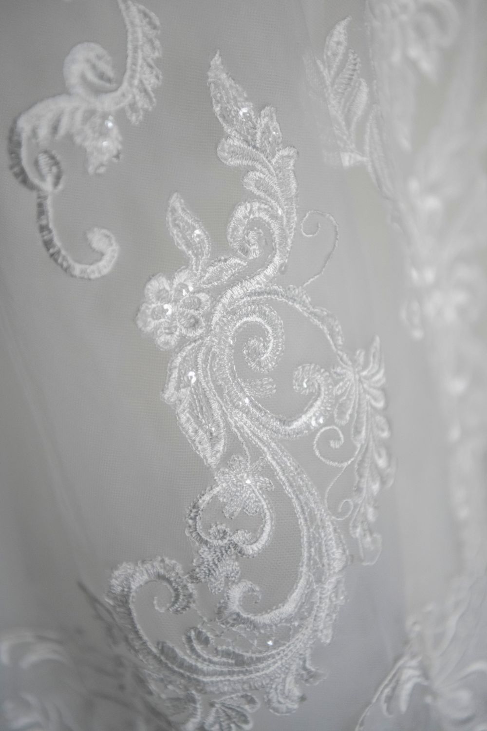 Delicate white lace embroidery detail on wedding dress fabric shown in macro.
