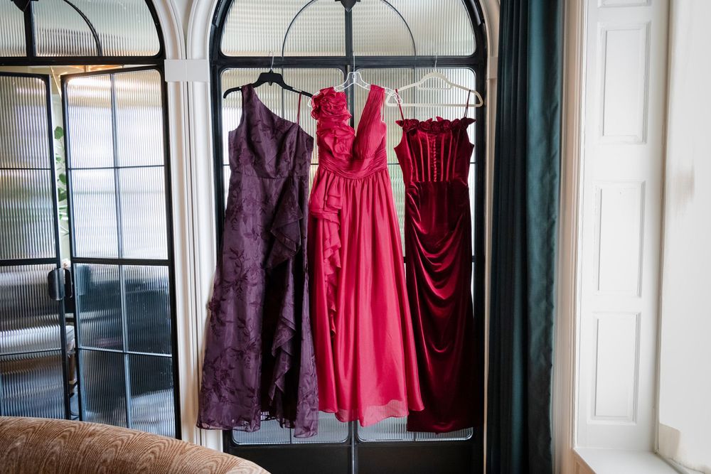 Elegant evening gowns and formal dresses hanging in a row against white walls with arched windows.