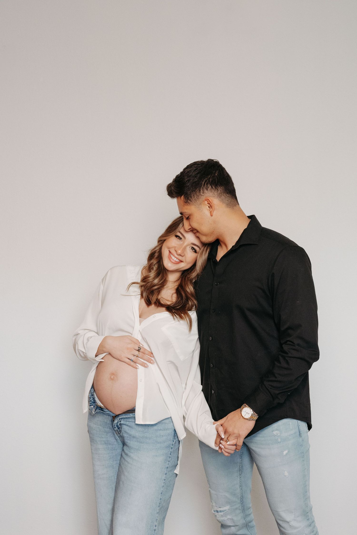 A couple in light jeans and contrasting black and white tops embrace in a minimalist studio setting.