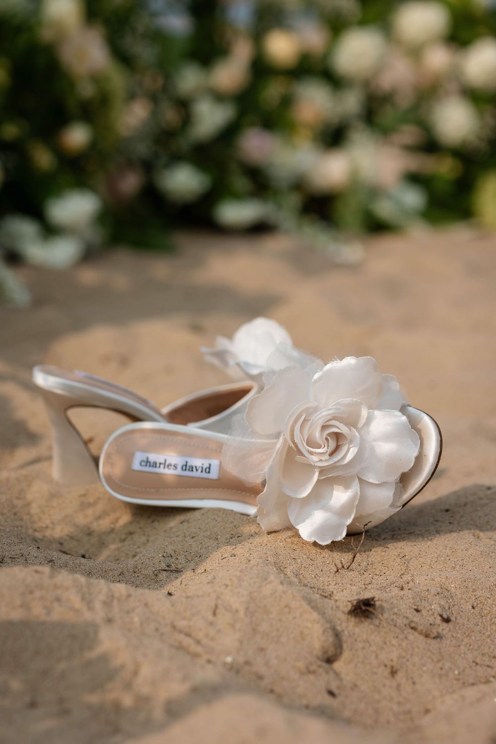 White seashell and delicate floral decorative elements arranged artistically on sandy beach background.