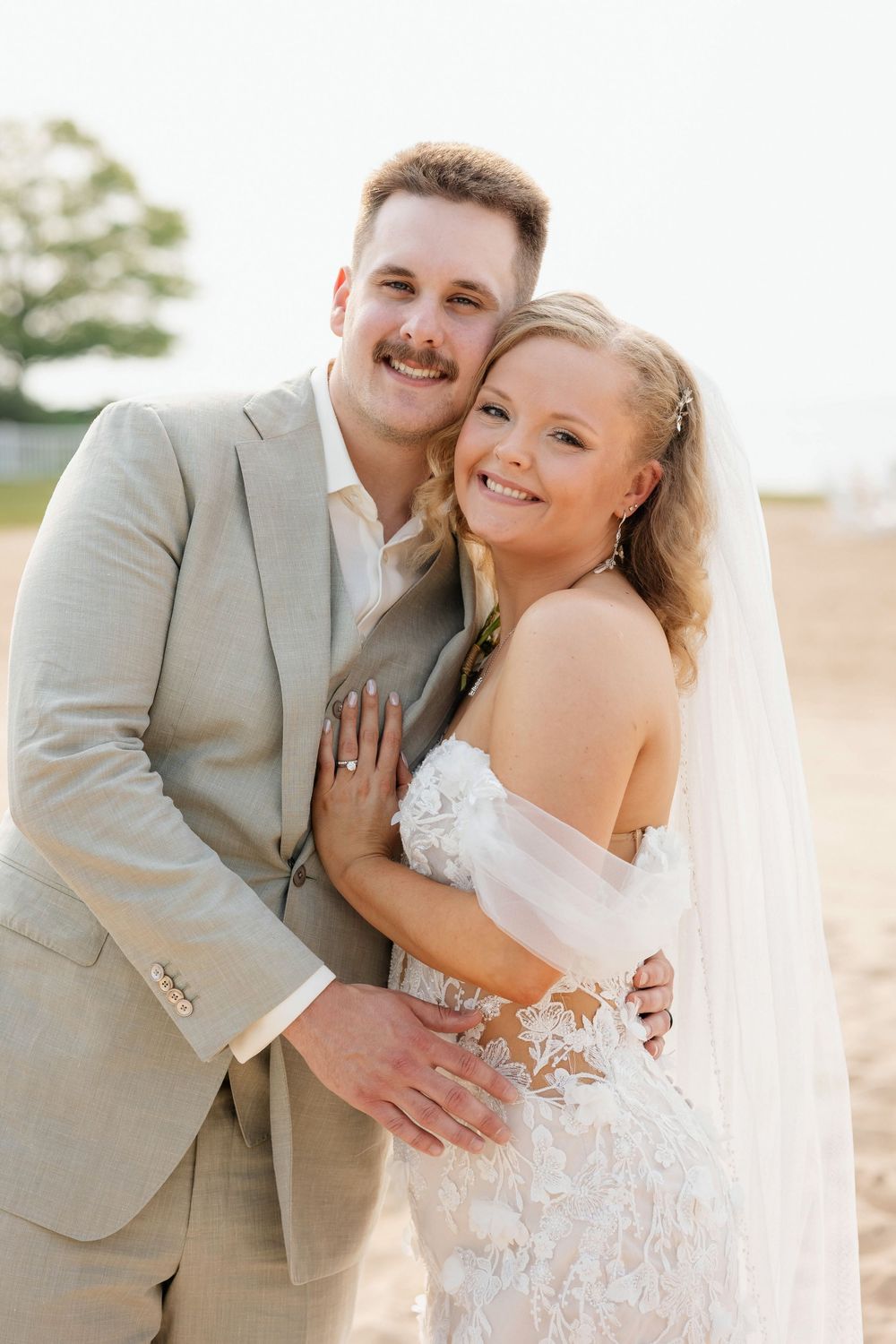 A romantic wedding couple embraces outdoors in beige and white attire during a golden hour photoshoot.