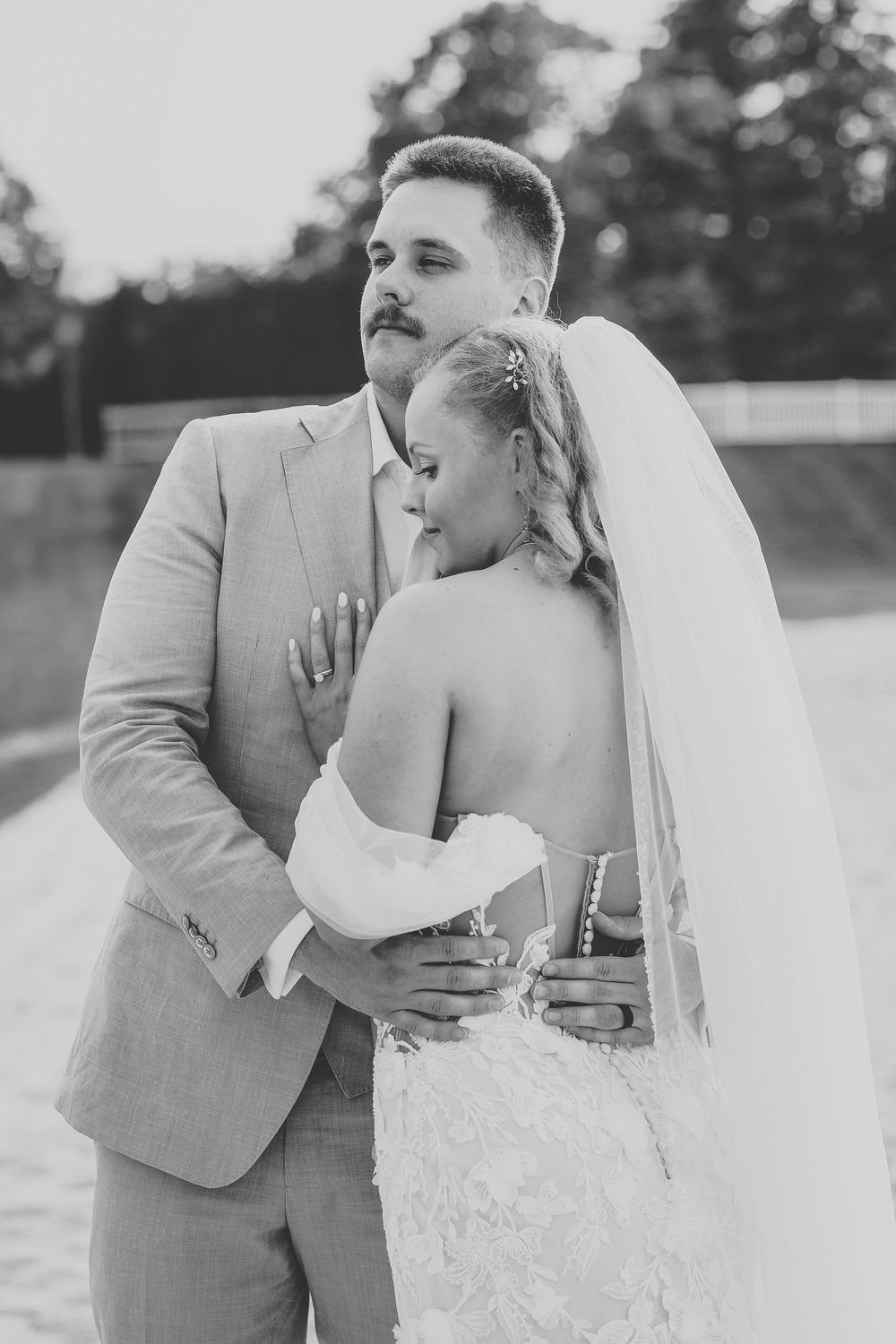 Black and white wedding photo showing a tender embrace between newlyweds, with the bride in a strapless gown and groom in light suit.