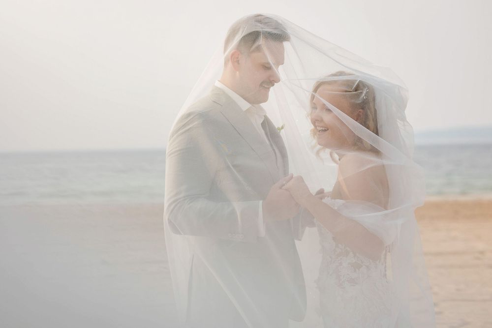 Romantic wedding couple embraces on a sandy beach during golden hour with mountains in the background.
