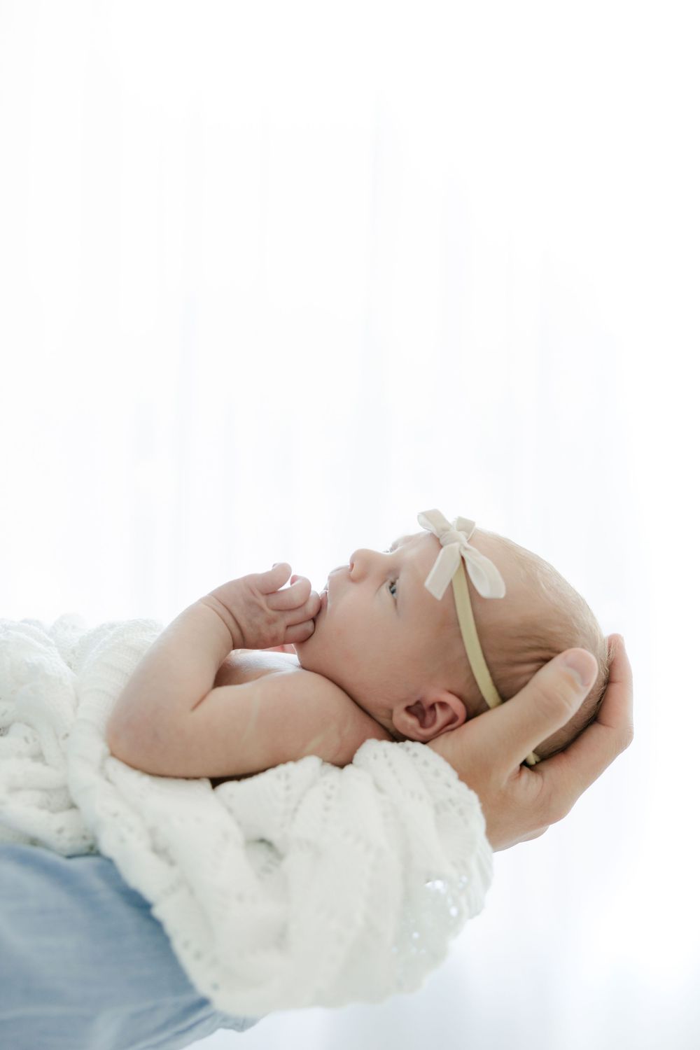 A baby lies on white blankets in a series of peaceful sleeping poses against a bright backdrop.