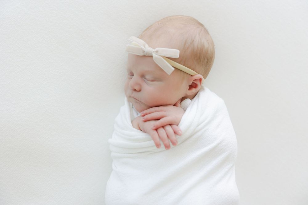 A sleeping newborn wrapped in soft white fabric rests peacefully against a light background.