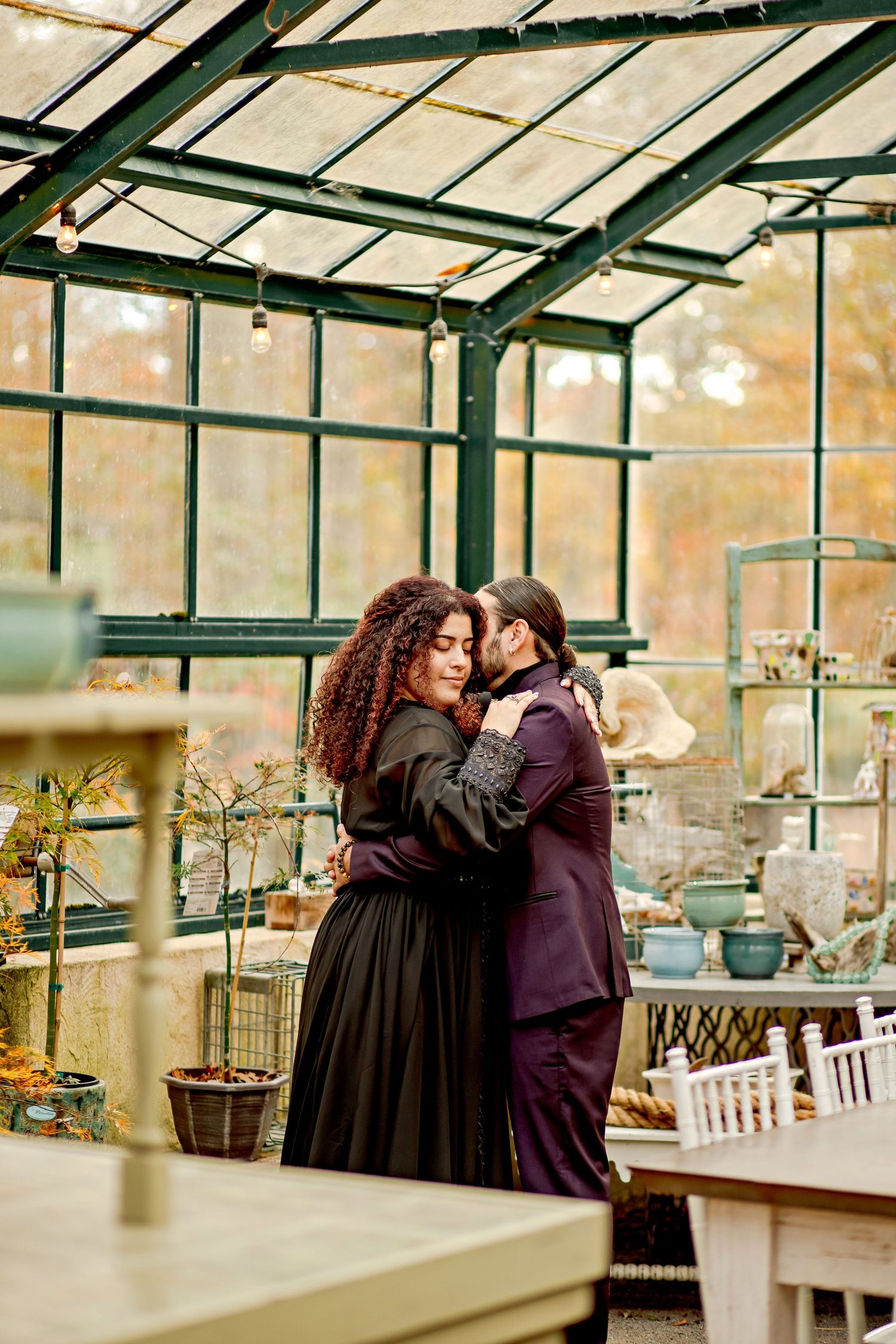 A couple embraces lovingly on a dirt path beside tall ornamental grasses on an overcast afternoon.