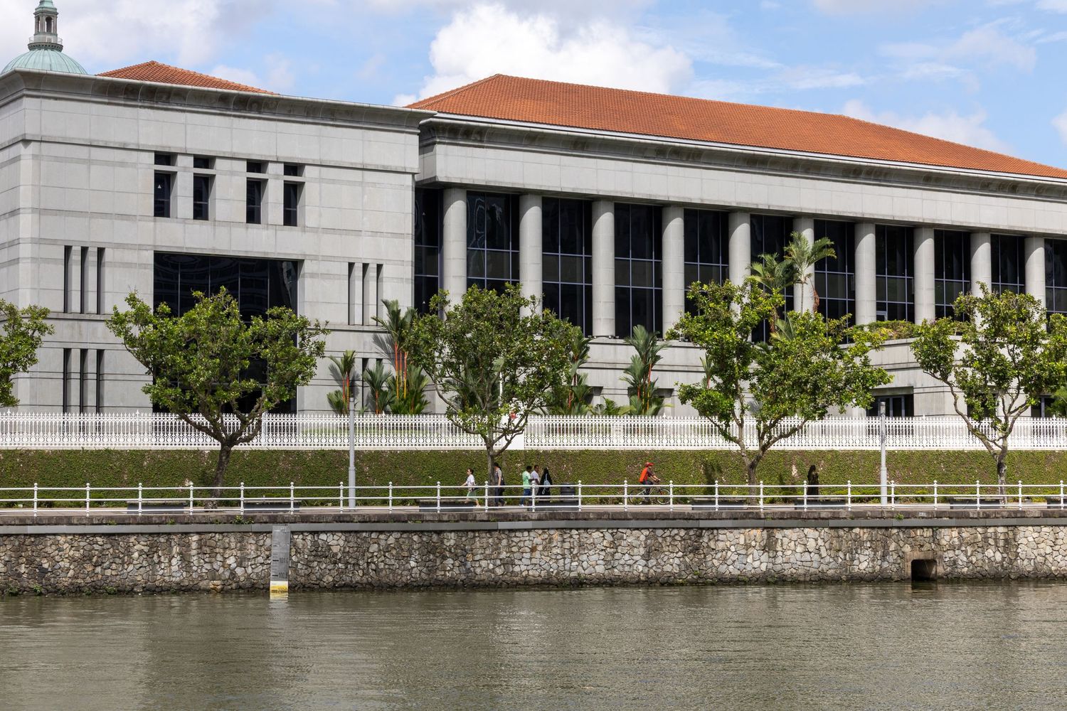 A panoramic view of a modern university building with orange tiled roof and white walls along a stone embankment.