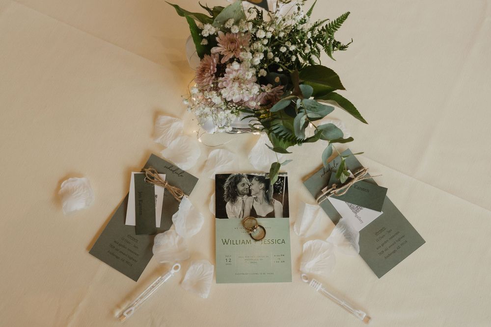 Elegant wedding stationery flat lay with sage green invitations, floral bouquet, and ribbon details.
