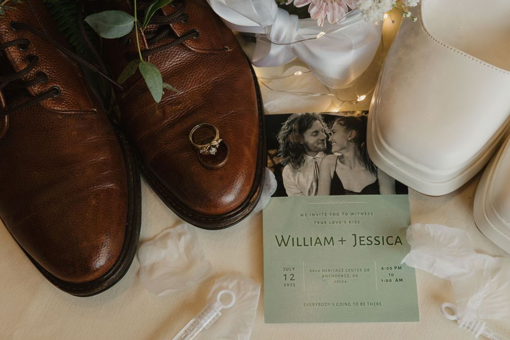 Wedding detail flat lay featuring brown leather dress shoes, gold ring, and William and Jessica invitation.
