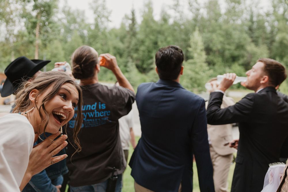 Wedding guests celebrating outdoors surrounded by lush green trees at a summer wedding reception.