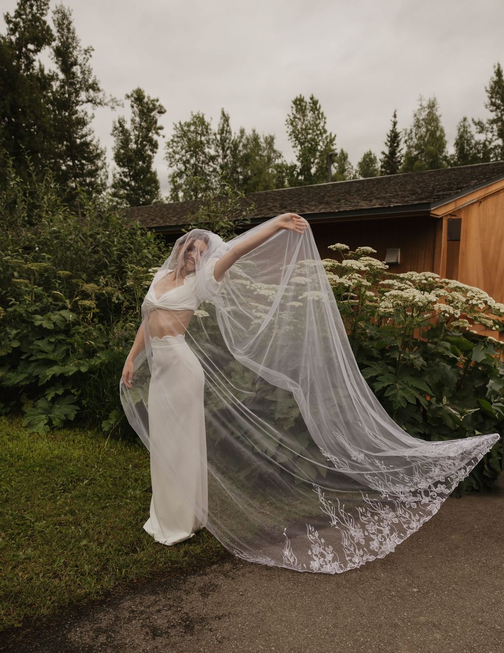 Bride in white gown twirling her long lace-trimmed cathedral veil outdoors at her wedding.