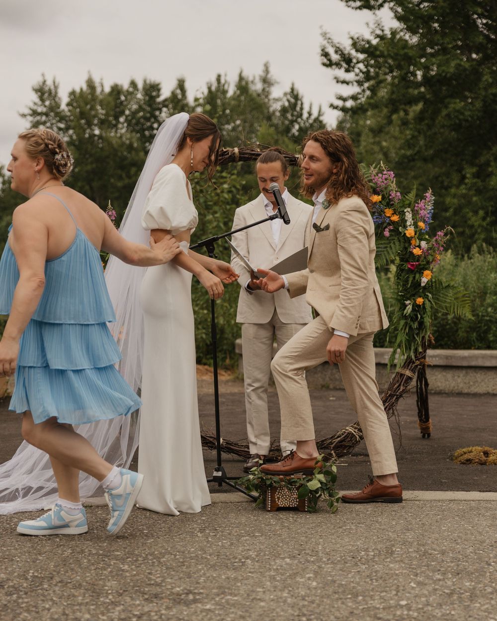 Bride and groom exchange vows outdoors at a colorful floral arch wedding ceremony with bridal party.