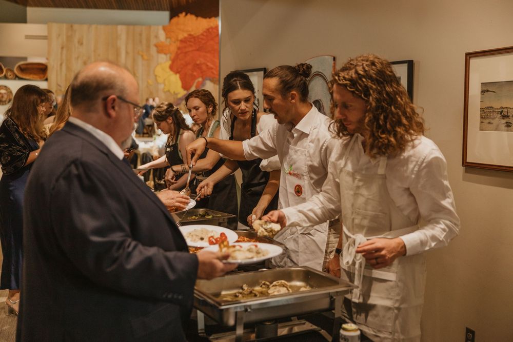Wedding guests being served food at a buffet reception by catering staff in white uniforms.