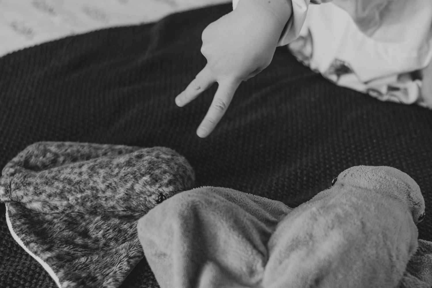 Black and white photo of a baby hand reaching toward folded socks on a dark textured blanket | Annual Birthday Photos for Kids