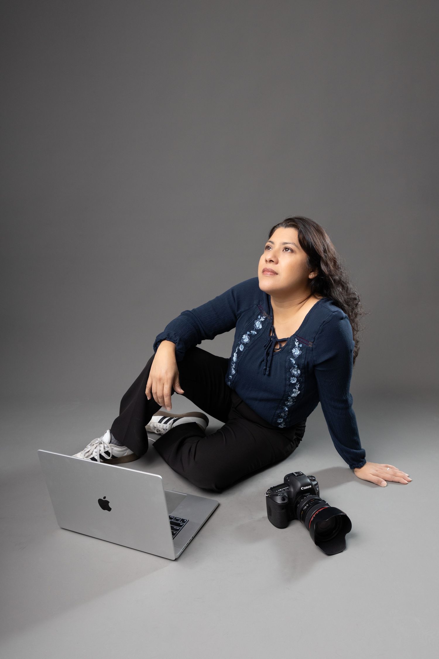 A dancer in dark jeans and navy top strikes a dynamic pose against a gray studio backdrop.