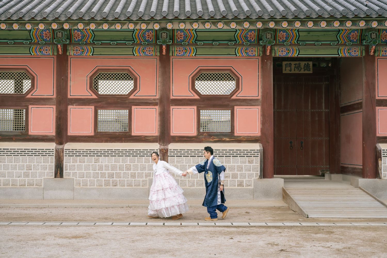 Traditional Korean palace architecture with people walking along covered walkways and ornate wooden buildings.