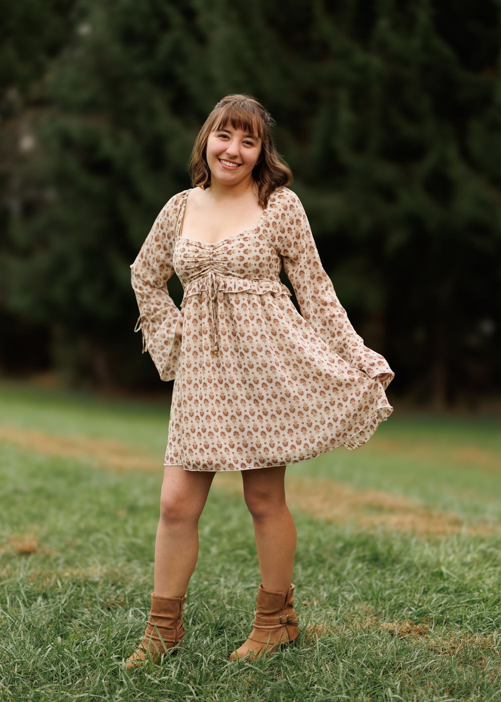 A floral prairie dress with brown boots photographed on green grass in a casual outdoor setting.
