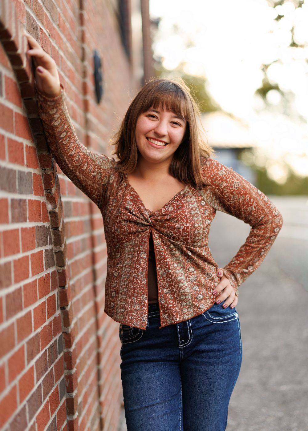 Person in sparkly brown top posing against brick wall during golden hour.