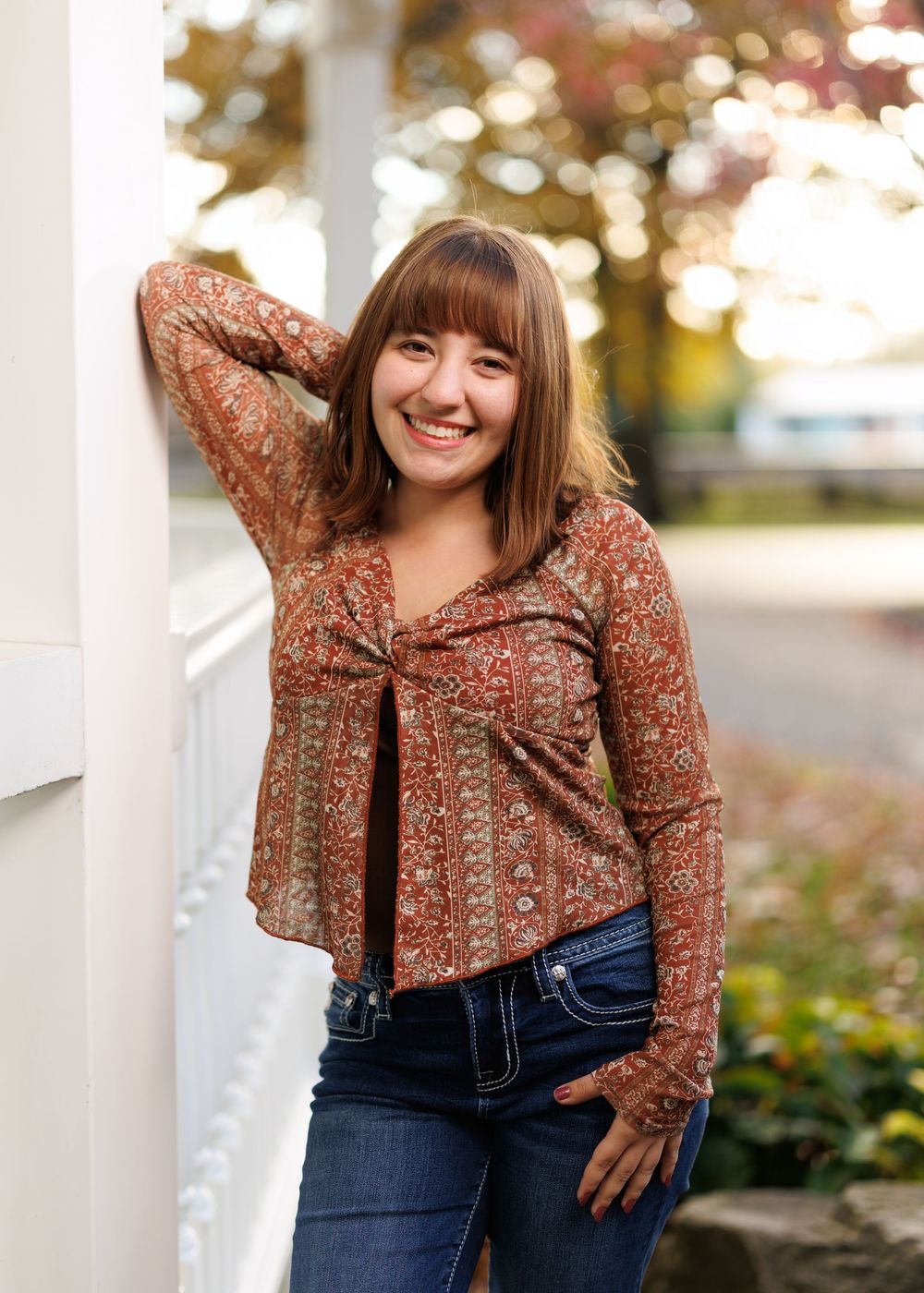 A casual autumn outfit featuring a patterned top and dark jeans photographed near white columns.
