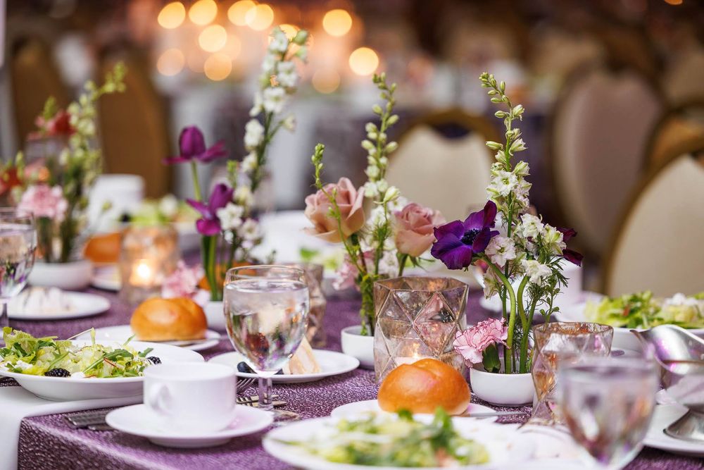 Elegant wedding reception table settings with purple accents, floral centerpieces and glowing candlelight create a romantic ambiance.