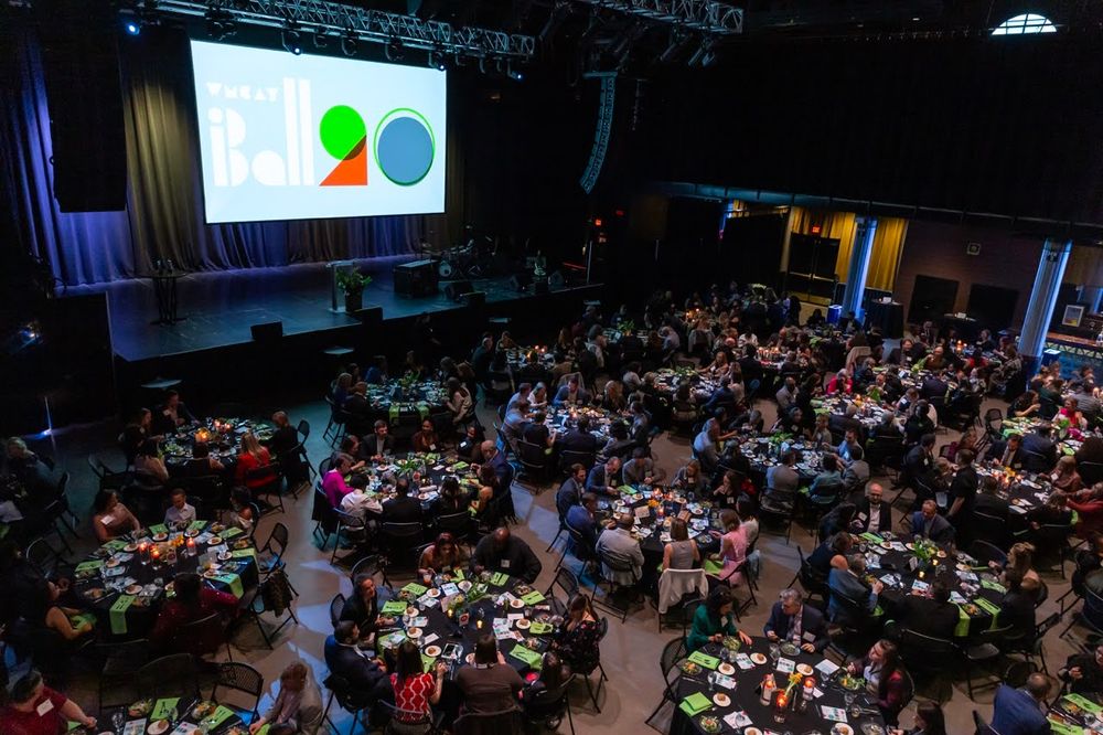 A large crowd fills a dimly lit auditorium during a conference or presentation event.