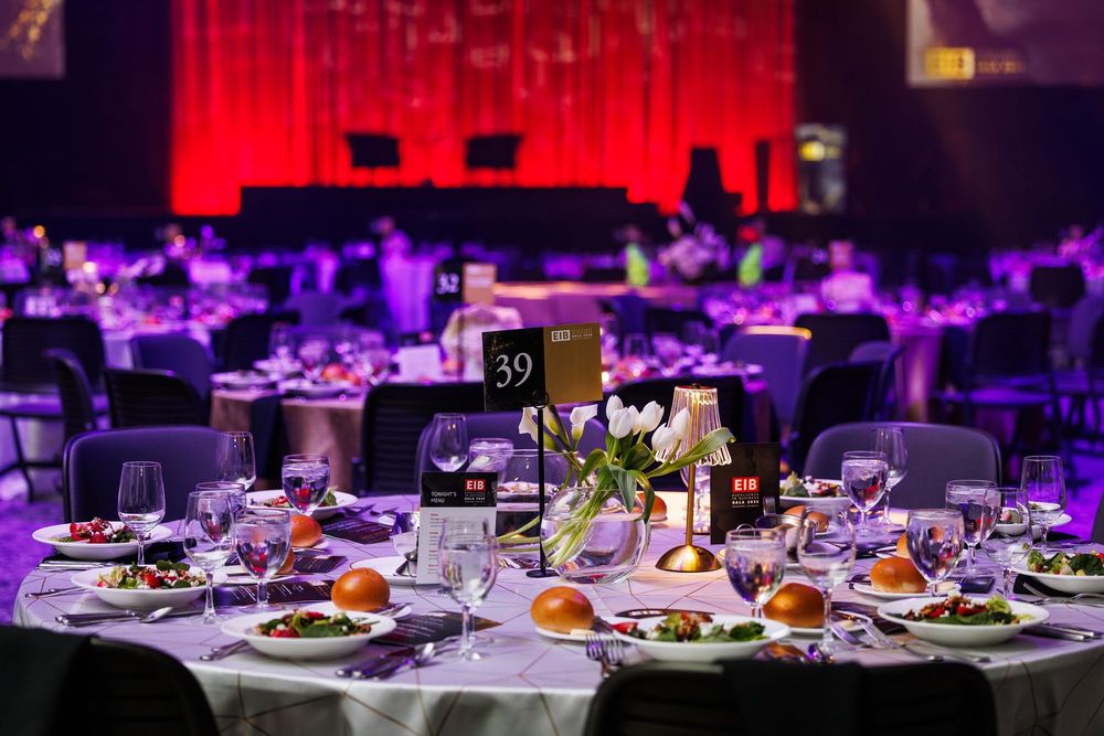 Elegant banquet tables set with white linens and purple ambient lighting create a sophisticated dining atmosphere.
