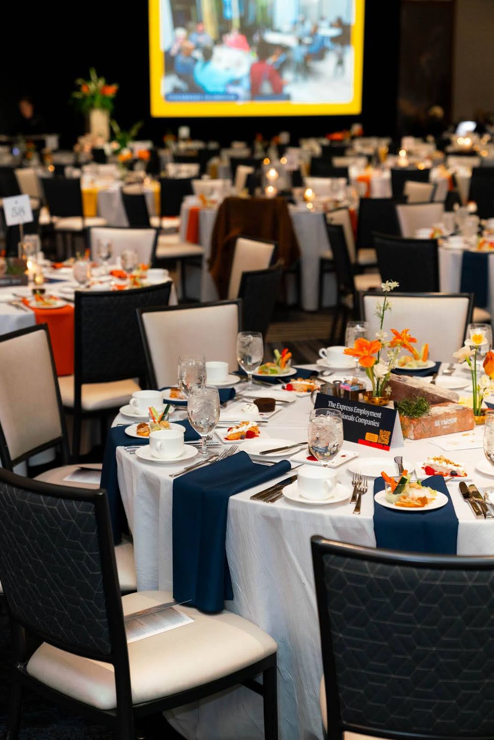 Elegant banquet tables set with white linens, navy blue accents, and colorful floral centerpieces in an upscale dining room.