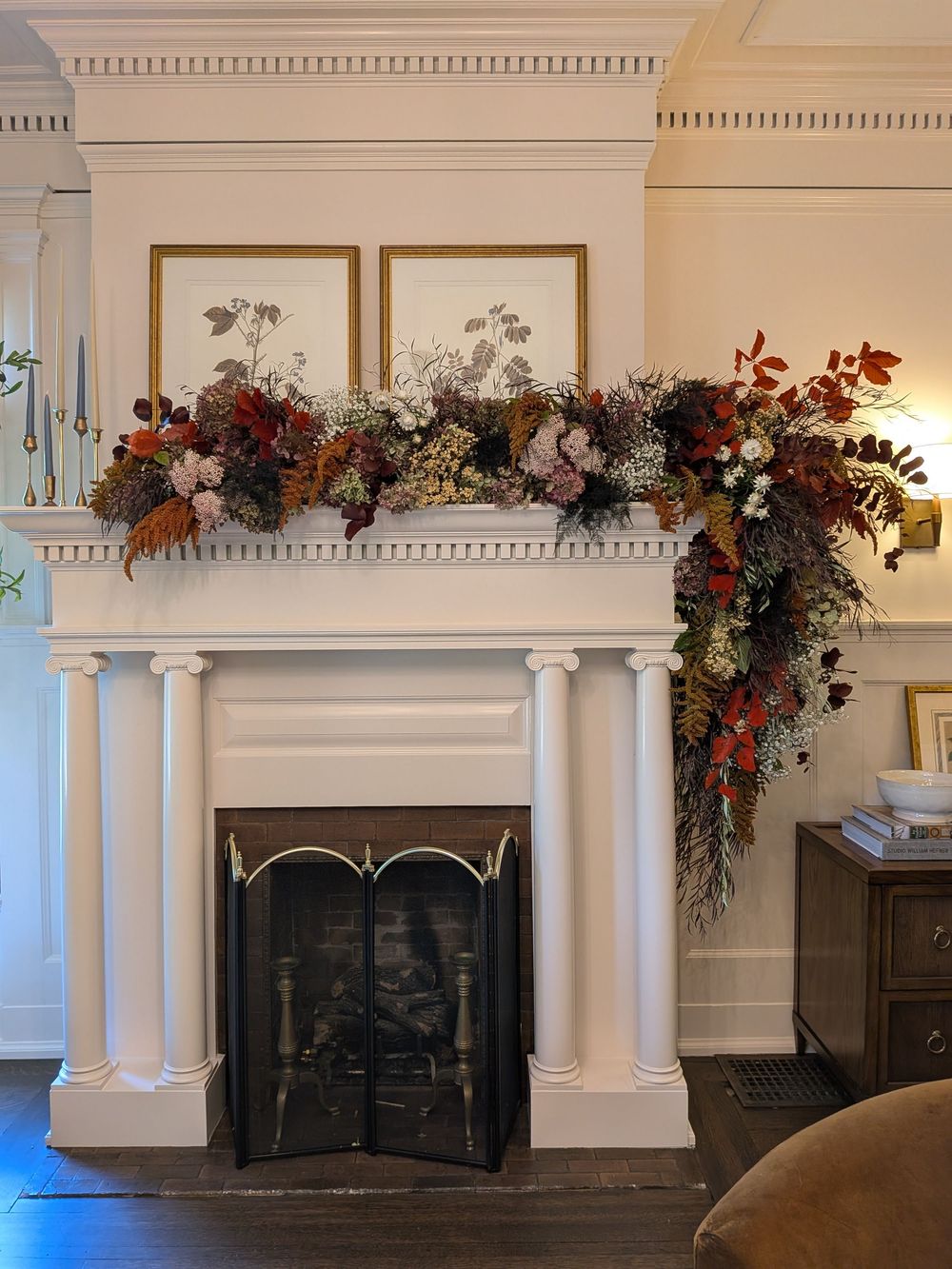 Elegant white fireplace mantel decorated with cascading autumn floral arrangements and greenery in a formal room.