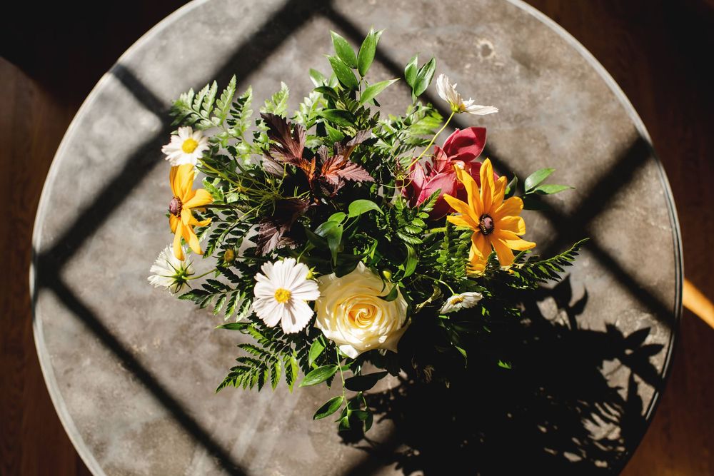 Fresh floral arrangement with vibrant orange, yellow and white blooms alongside green foliage on a gray surface.