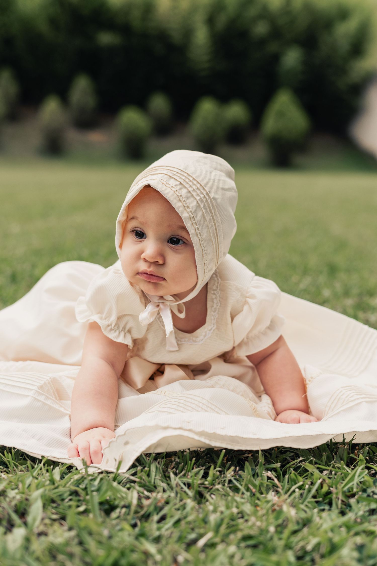 A baby in a white bonnet and dress lying on green grass in a series of connected outdoor photos.