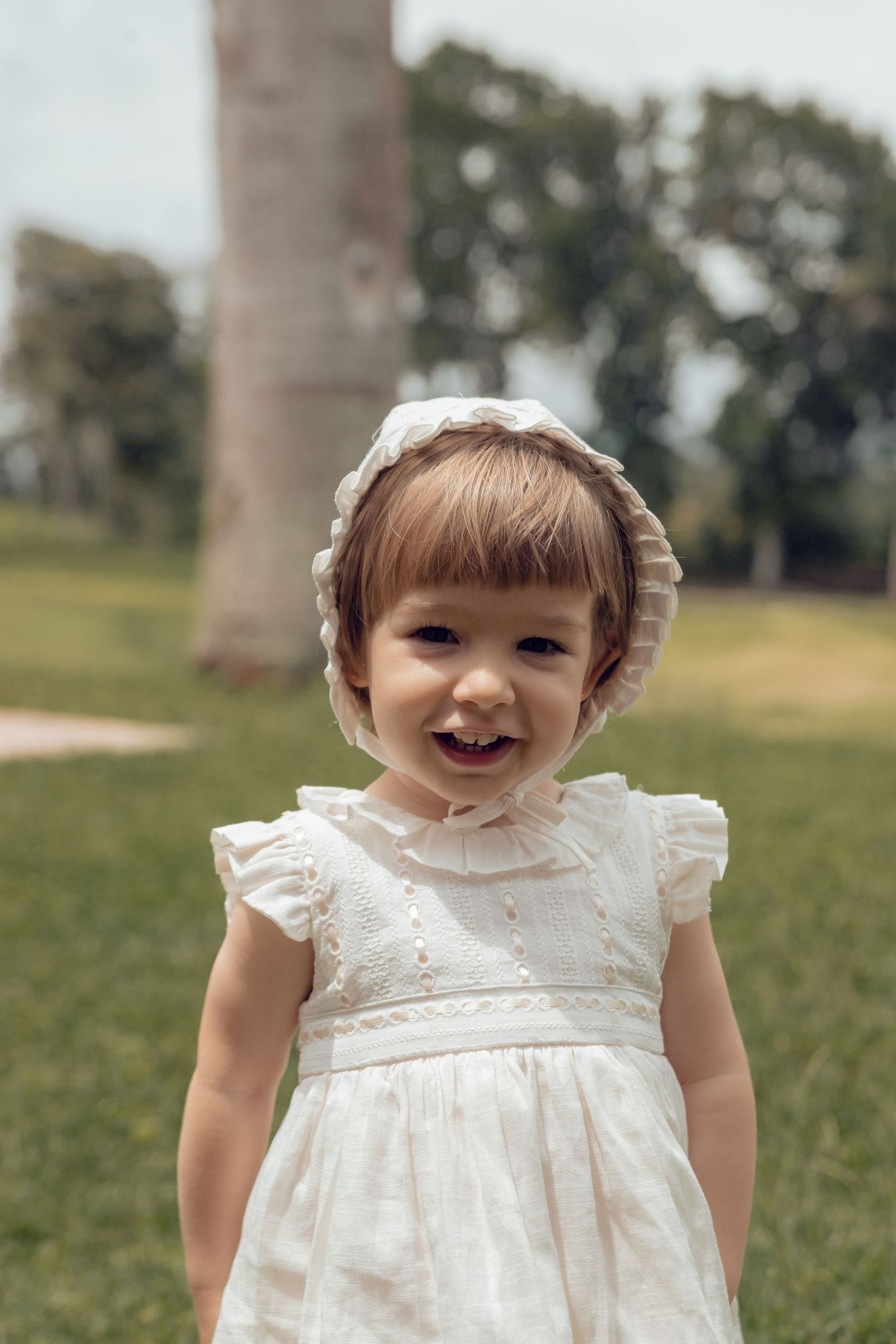 A small child wearing a white ruffled dress playing outdoors on a grassy lawn.