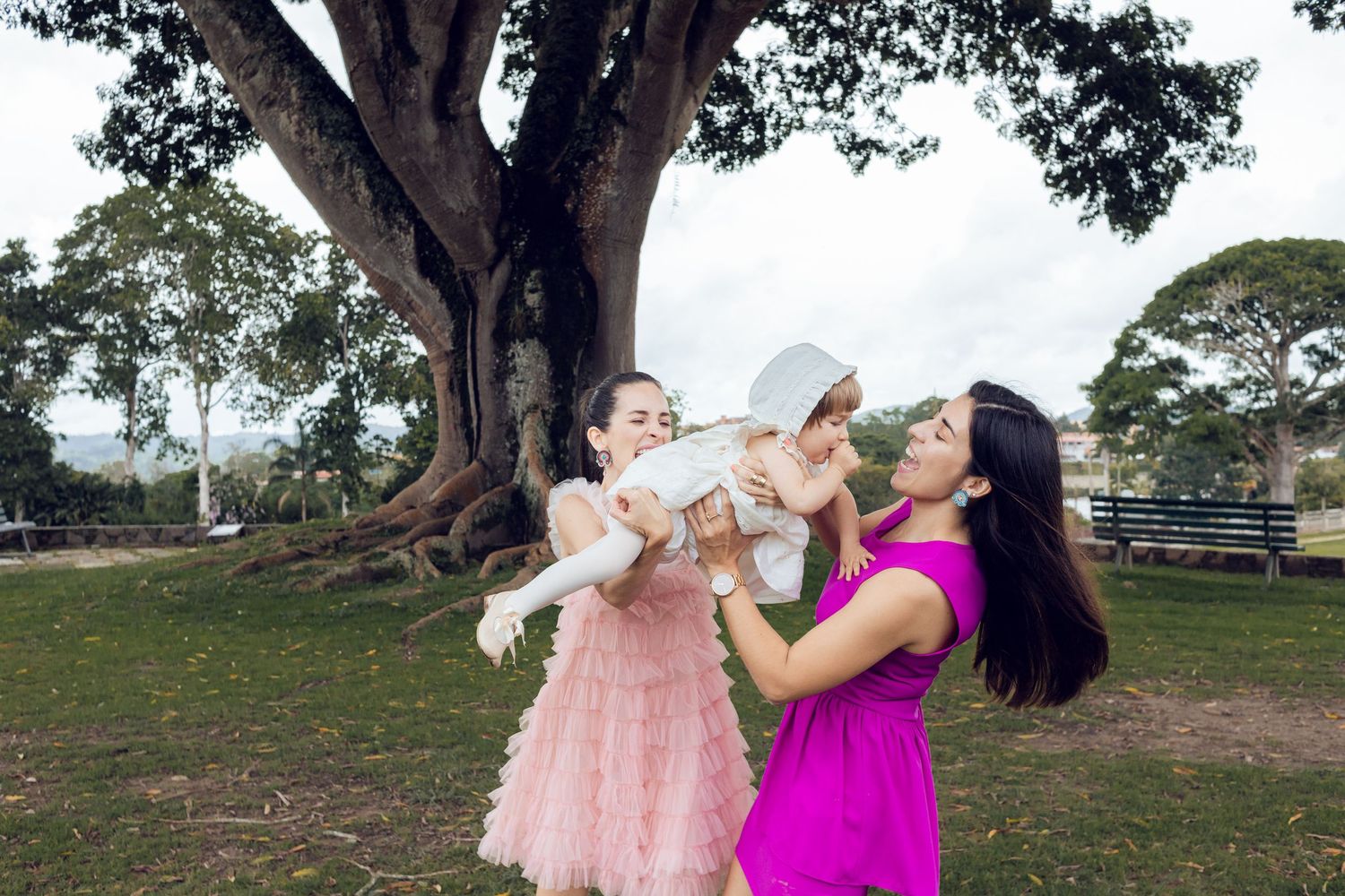 Mother and child playing together under large trees in a park setting during sunset.