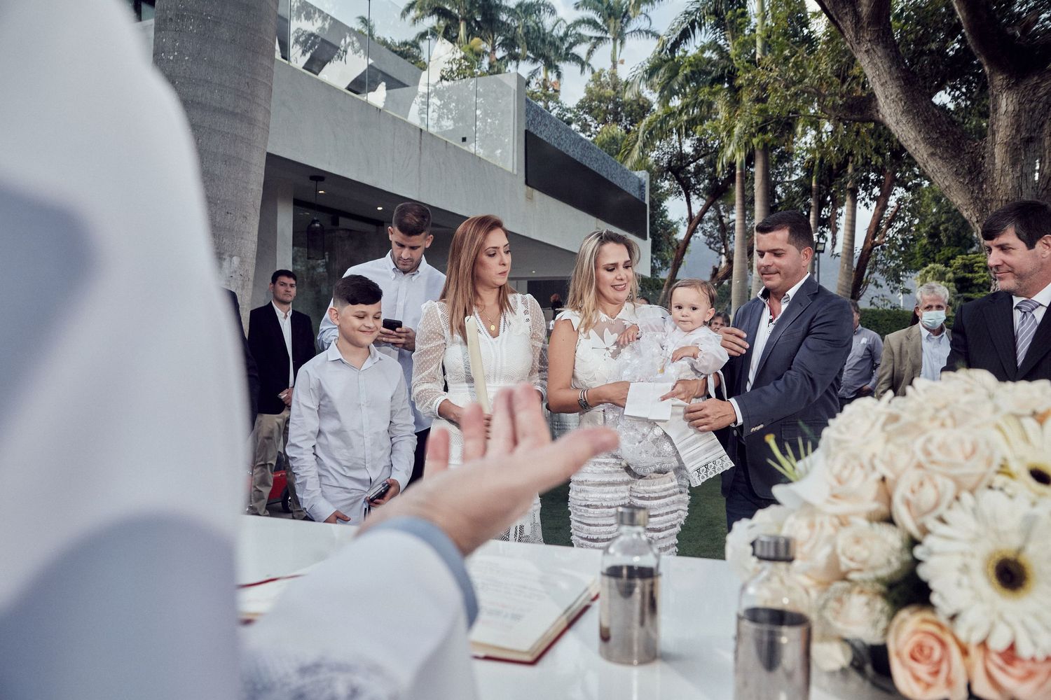 Elegant outdoor wedding reception setup with palm trees and white floral arrangements on tables.